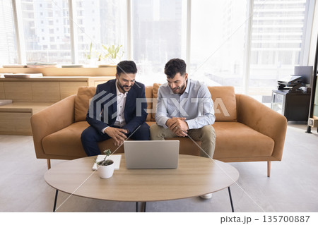 Two happy young businessmen watch video presentation on notebook screen 135700887