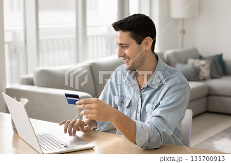 Smiling young man pay online from credit card using notebook Smiling young man pay online from credit card using notebook 135700913