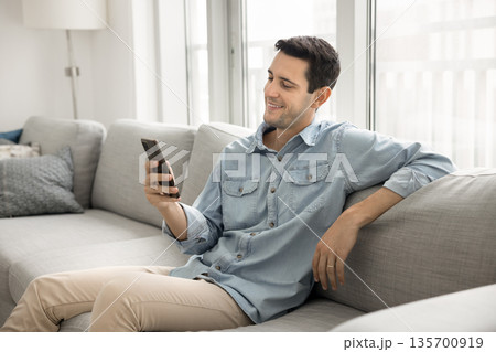 Happy young man spend time relaxing on sofa with phone Happy young man spend time relaxing on sofa with phone 135700919