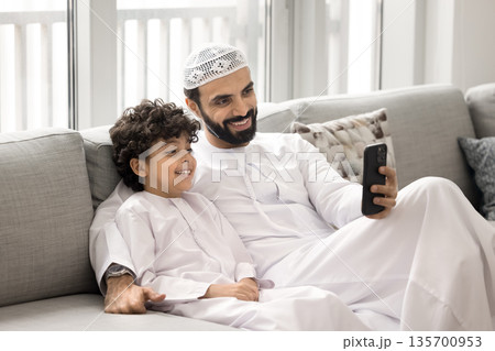 Young Arabic father and child son using phone on sofa 135700953
