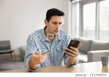 Stressed millennial male hold phone credit card look at screen 135700974
