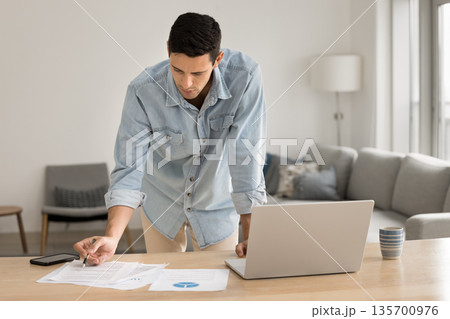 Young male financial analyst reviewing paper documents at home office Young male financial analyst reviewing paper documents at home office 135700976