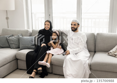 Happy Arabic parents and daughter preschooler watch tv on couch Happy Arabic parents and daughter preschooler watch tv on couch 135700988
