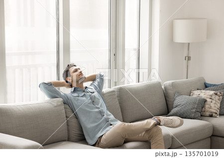 Carefree young guy lying back on sofa with eyes closed 135701019