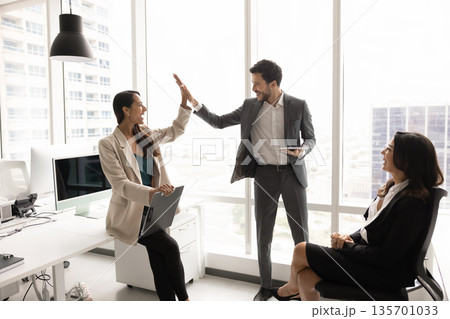 Two happy teammates exchanging high-five gesture in coworking office 135701033