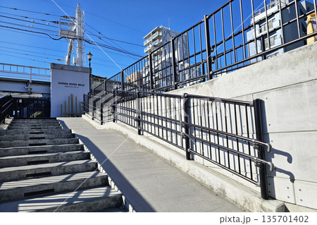 Entrance to the Sumida River Walk pedestrian pathway with stairs and ramp on a sunny day. 135701402