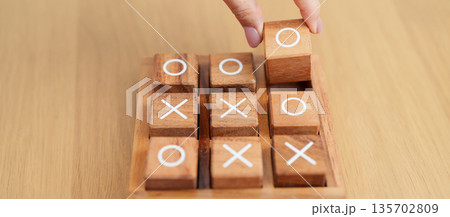 Hand holding and playing wooden block of tic tac toe game. A completed game of noughts and crosses or Xs and Os game. Challenge, Competition, winning, tactic, strategy and recreation concepts Hand holding and playing wooden block of tic tac toe game. A completed game of noughts and crosses or Xs and Os game. Challenge, Competition, winning, tactic, strategy and recreation concepts 135702809