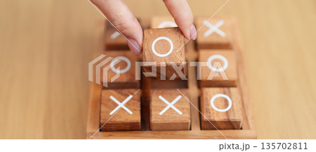 Hand holding and playing wooden block of tic tac toe game. A completed game of noughts and crosses or Xs and Os game. Challenge, Competition, winning, tactic, strategy and recreation concepts Hand holding and playing wooden block of tic tac toe game. A completed game of noughts and crosses or Xs and Os game. Challenge, Competition, winning, tactic, strategy and recreation concepts 135702811