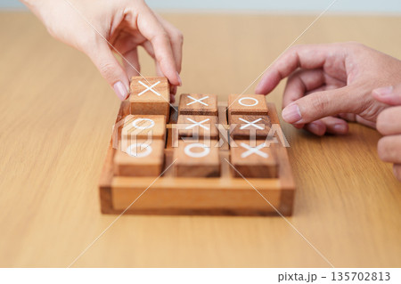 Hand holding and playing wooden block of tic tac toe game. A completed game of noughts and crosses or Xs and Os game. Challenge, Competition, winning, tactic, strategy and recreation concepts Hand holding and playing wooden block of tic tac toe game. A completed game of noughts and crosses or Xs and Os game. Challenge, Competition, winning, tactic, strategy and recreation concepts 135702813