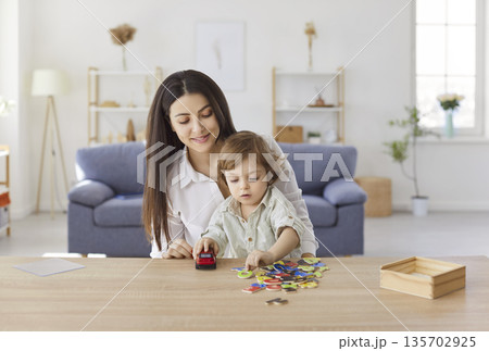 Smiling mother playing with little son at desk, learning alphabet and enjoying fun time at home. 135702925