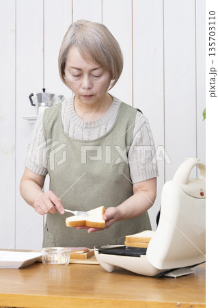 ホットサンドメーカーでホットサンドを作るシニア女性 ホットサンドメーカーでホットサンドを作るシニア女性 135703110