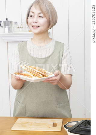 ホットサンドメーカーでホットサンドを作るシニア女性 135703128