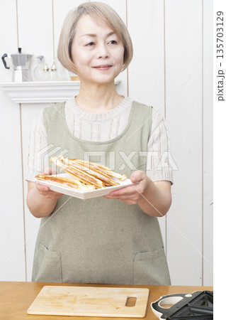 ホットサンドメーカーでホットサンドを作るシニア女性 ホットサンドメーカーでホットサンドを作るシニア女性 135703129
