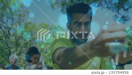 Punching adult Indian man wearing neon green shirt and smartwatch, in leafy park fitness class 135704956