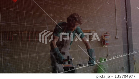 Sanding artisan wearing apron using power sander on wood plank in garage, digital grid overlay 135704977