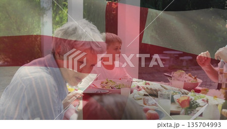 Sharing family passing salad bowls around wooden table beneath white pergola, with fruit and milk 135704993