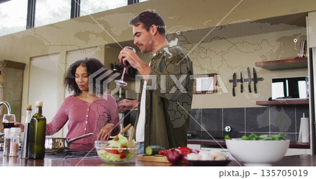 Couple cooking together stirring vegetables and sipping wine at kitchen island, with frying pan 135705019