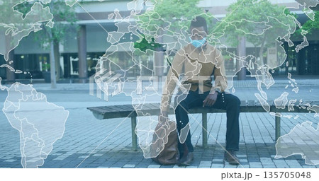 Sitting male wearing face mask, tan shirt beside backpack on plaza bench, with world map overlay 135705048