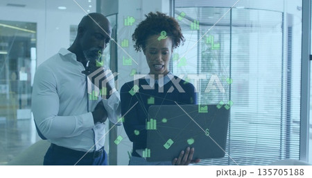 Reviewing green financial charts on laptop, professionals standing by glass partition in office Reviewing green financial charts on laptop, professionals standing by glass partition in office 135705188
