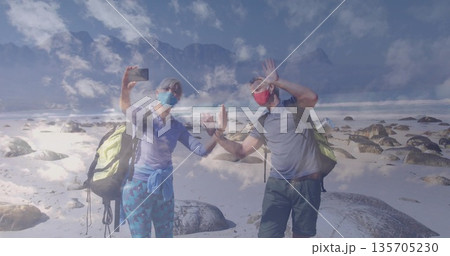Waving friends wearing masks taking selfie on shore at mountain, smartphone and hiking backpacks Waving friends wearing masks taking selfie on shore at mountain, smartphone and hiking backpacks 135705230