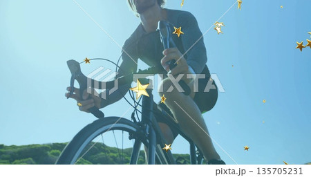 Pedaling road bicyclist gripping drop handlebars on road beside hills under blue sky, golden stars 135705231