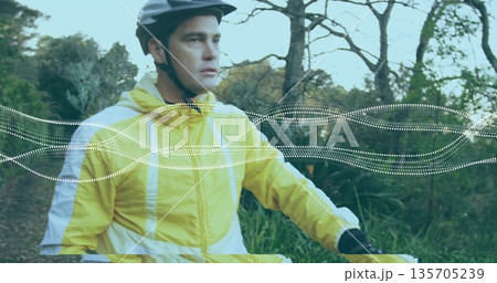 Riding light-skinned cyclist pedaling forest trail, with helmet, windbreaker, handlebars and gloves Riding light-skinned cyclist pedaling forest trail, with helmet, windbreaker, handlebars and gloves 135705239