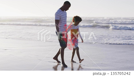 Walking mid adult man and boy strolling along sandy shoreline, with wet sand reflecting ocean waves 135705242