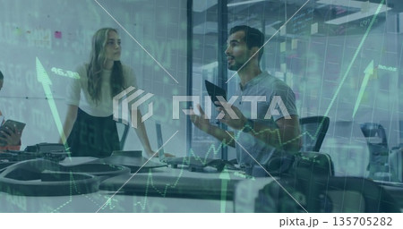 Standing man in gray polo holding tablet, gesturing in conference room with laptop, phones, graphs Standing man in gray polo holding tablet, gesturing in conference room with laptop, phones, graphs 135705282