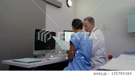 Reviewing nurse and doctor consulting patient charts in clinic exam room, with computer monitors 135705384