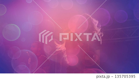 Performing female musician singing into microphone on stage, with purple-pink lighting and trusses Performing female musician singing into microphone on stage, with purple-pink lighting and trusses 135705395