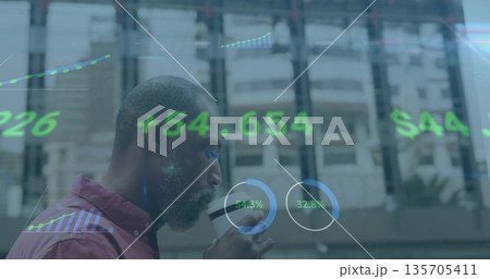 Standing African American man in burgundy shirt sipping coffee at urban glass wall with data charts Standing African American man in burgundy shirt sipping coffee at urban glass wall with data charts 135705411