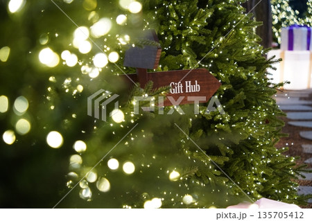 Wooden Gift Hub Sign Amidst Twinkling Christmas Tree Lights and Festive Decorations Wooden Gift Hub Sign Amidst Twinkling Christmas Tree Lights and Festive Decorations 135705412