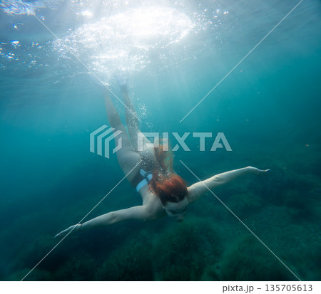 Underwater woman diving through clear turquoise ocean water as sunbeams shine from the surface promoting freedom and adventure in nature Underwater woman diving through clear turquoise ocean water as sunbeams shine from the surface promoting freedom and adventure in nature 135705613
