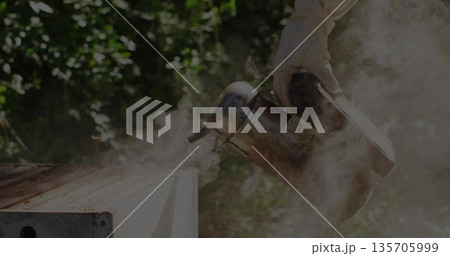 Holding gloved hand gripping metal smoker emitting smoke over wooden hive box in garden, copy space 135705999