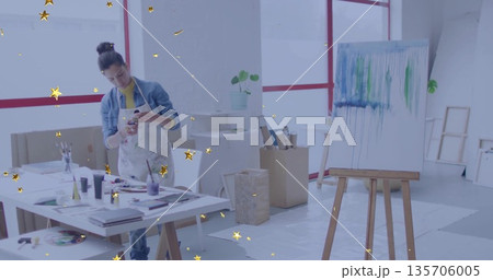Holding smartphone, female artist in paint apron examining canvas drips at art studio, with easel Holding smartphone, female artist in paint apron examining canvas drips at art studio, with easel 135706005