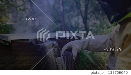 Beekeeper in suit manipulating hive tool beside wooden hive box at apiary, metal smoker, copy space 135706040