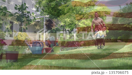 Gardening family tending plants, pushing child in wheelbarrow in suburban front yard, watering can 135706075