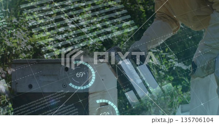 Gloved beekeeper operating metal smoker beside hive box in apiary with data lines, copy space Gloved beekeeper operating metal smoker beside hive box in apiary with data lines, copy space 135706104
