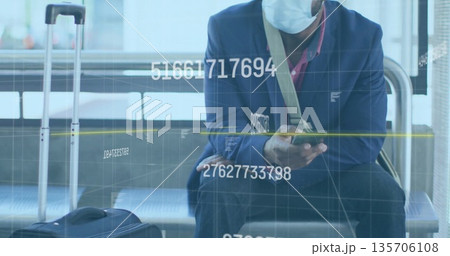 Checking smartphone man wearing suit and mask sitting at airport with suitcase and bag amid overlay 135706108