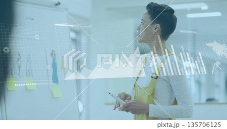 Woman in yellow overalls using stylus annotating whiteboard in office, with data charts, copy space Woman in yellow overalls using stylus annotating whiteboard in office, with data charts, copy space 135706125