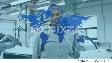 Standing mechanic wearing gray coverall in garage, silver car on car lift and world map overlay 135706197