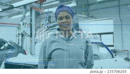 Black technician wearing coveralls and patterned scarf inspecting chassis in workshop, with lift Black technician wearing coveralls and patterned scarf inspecting chassis in workshop, with lift 135706205