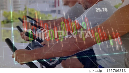 Spinning three men pedaling on spin bikes in spin studio by windows with financial chart overlay 135706218
