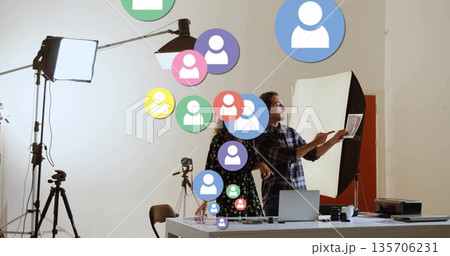 Pointing creators casual attire reviewing prints in studio with floating user icons, copy space 135706231