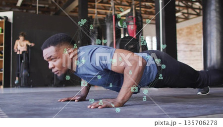 Man in blue athletic shirt black pants performing push-ups at gym, with floating health icons 135706278
