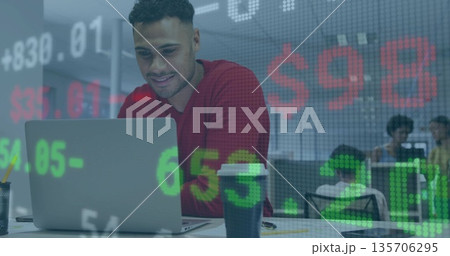 Hispanic man wearing red sweater analyzing stocks on laptop in open office, with coffee cup, pencil Hispanic man wearing red sweater analyzing stocks on laptop in open office, with coffee cup, pencil 135706295