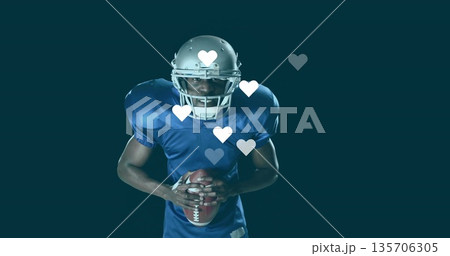 Player wearing silver helmet and blue jersey holding football in studio, with floating heart icons Player wearing silver helmet and blue jersey holding football in studio, with floating heart icons 135706305