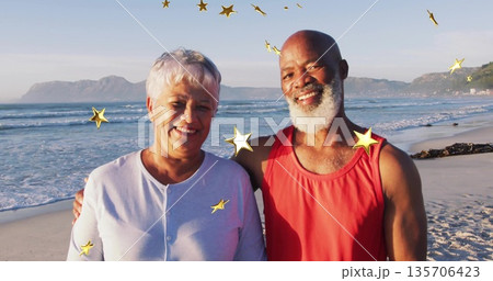 Smiling older couple standing on sandy shoreline, with golden star-shaped digital overlays 135706423