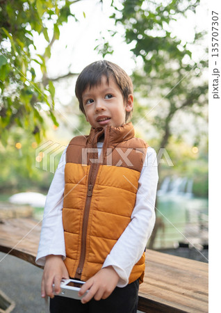 Boy Holding A Camera And Smiling In A Cozy Outdoor Setting Boy Holding A Camera And Smiling In A Cozy Outdoor Setting 135707307