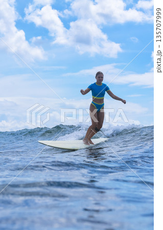 Woman Standing Proudly On Surfboard Amidst Turbulent Cloudy Backdrop 135707999